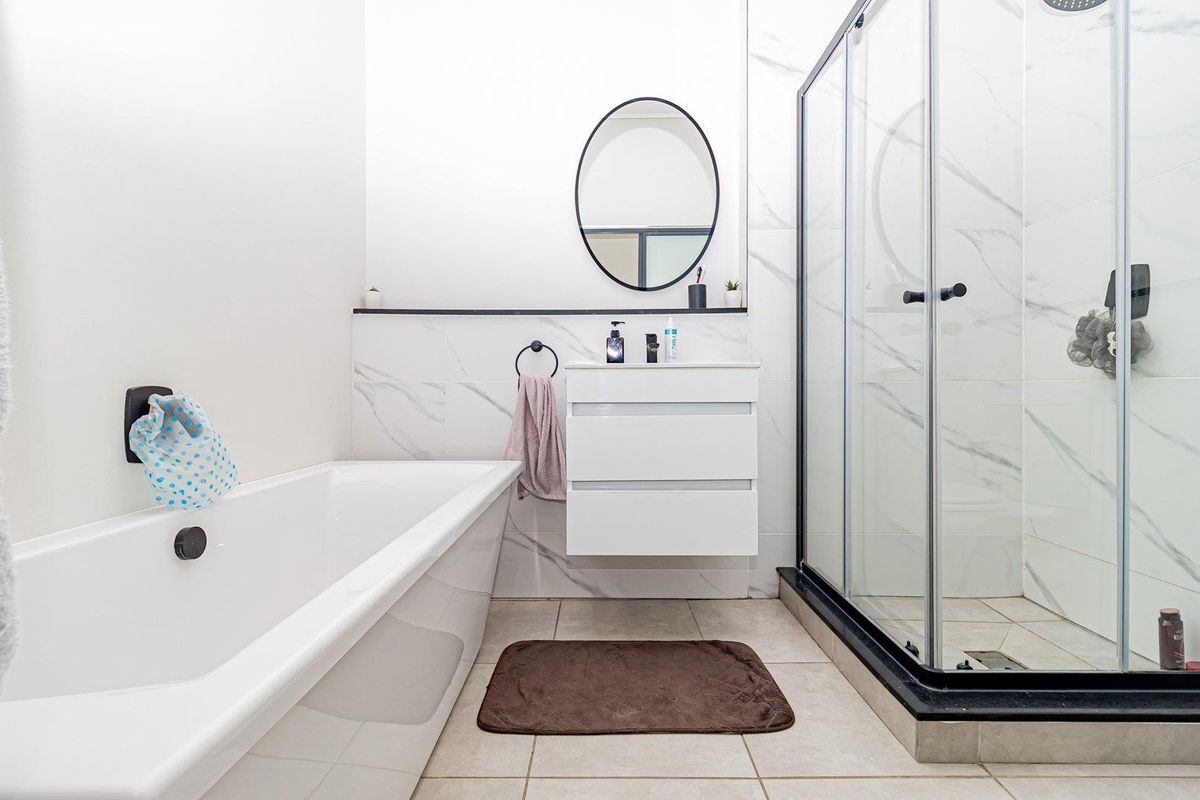 Modern bathroom featuring a sleek freestanding bathtub, a spacious walk-in shower with black fixtures, and a contemporary wall-mounted vanity with marble-look wall tiling.
