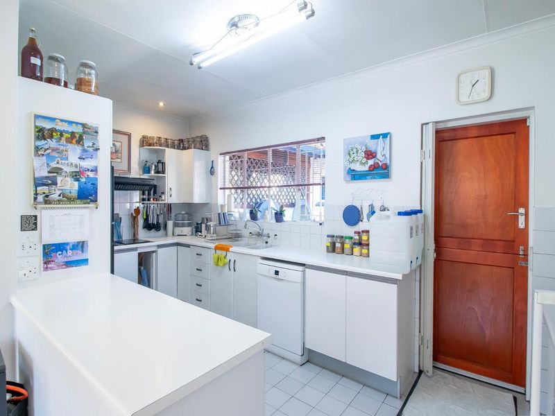 A functional kitchen featuring white built-in cabinetry, laminate countertops, tiled flooring, and a timber door leading to the exterior.