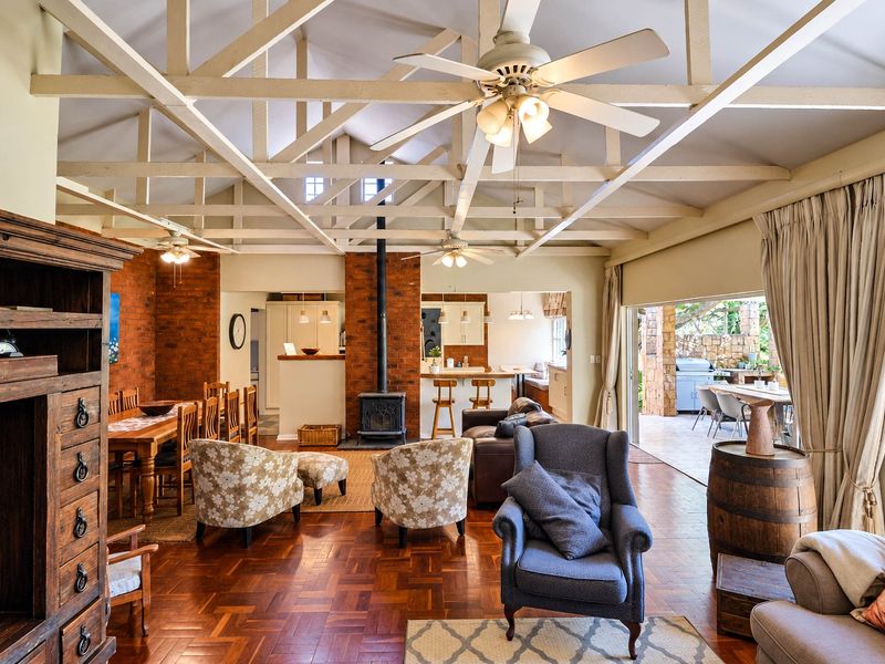 Spacious open-plan living and dining area featuring vaulted ceilings with exposed timber trusses, a central wood-burning fireplace, and seamless flow to the outdoor patio.