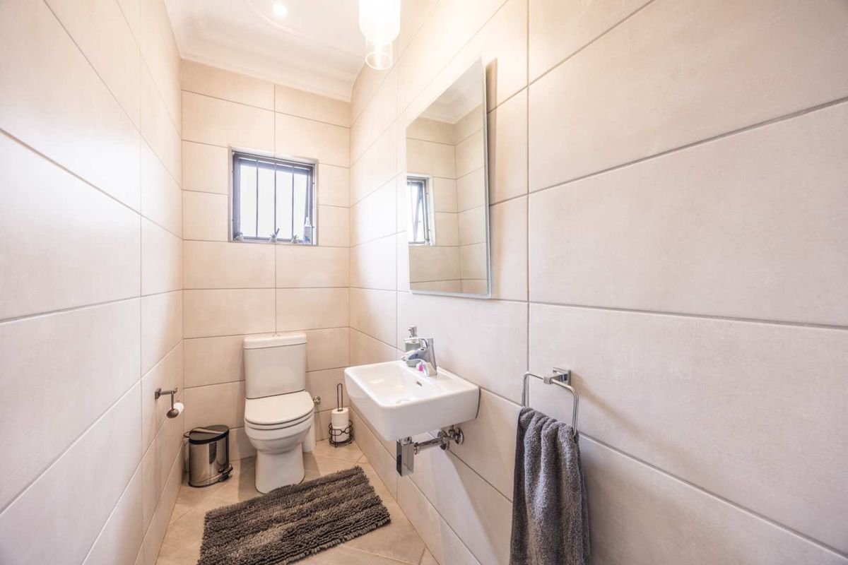 A clean, modern guest bathroom featuring neutral wall tiles, a wall-mounted basin with chrome fixtures, and a toilet.