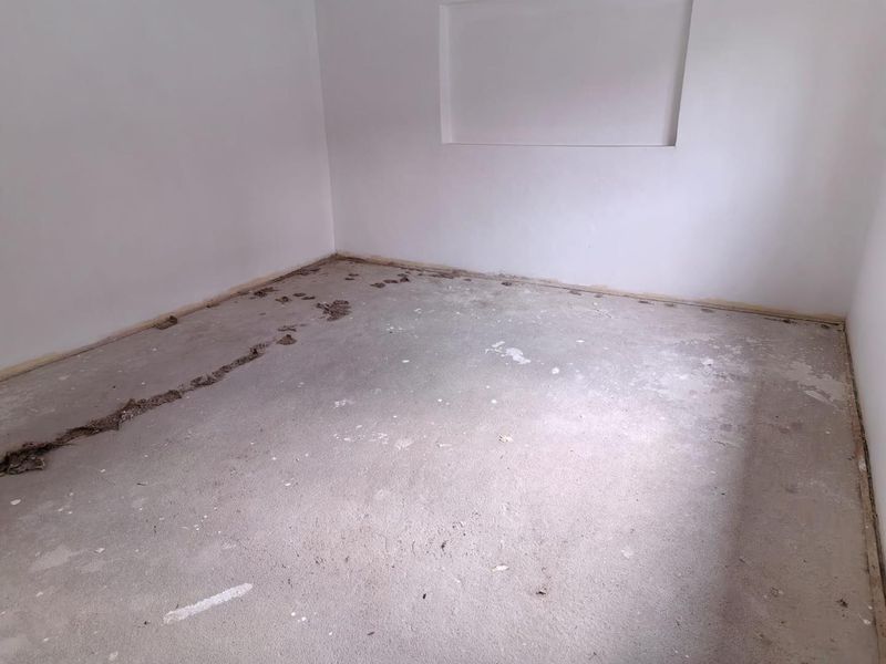 An empty, unfinished bedroom featuring white walls, a recessed wall niche, and a raw concrete floor awaiting final flooring installation.