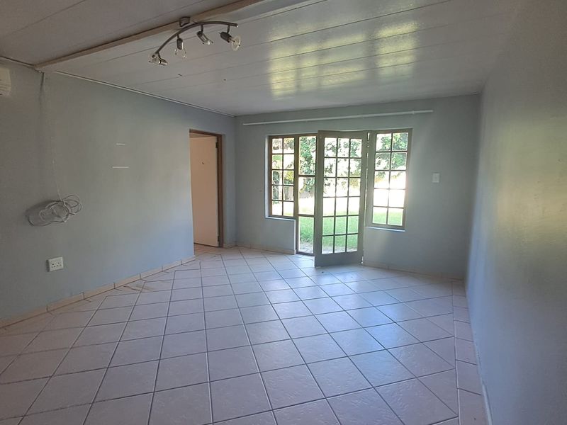 An empty living room featuring tiled flooring, ceiling track lighting, and french doors providing access to the garden area.