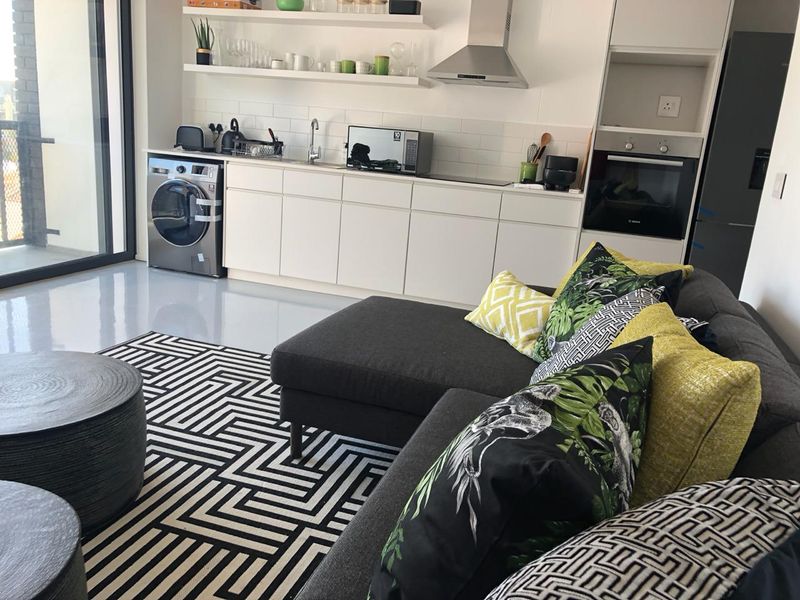 Modern open-plan living area featuring a sleek kitchen with built-in appliances, subway tile backsplash, floating shelves, and seamless epoxy flooring leading to a balcony.
