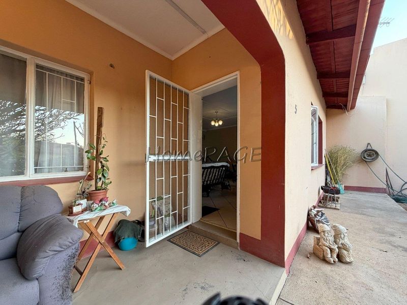 Covered patio area featuring concrete flooring, exposed rafters, and a security gate at the main entrance.