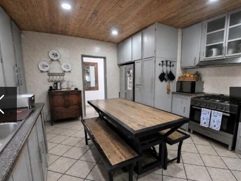 A functional kitchen featuring grey built-in cabinetry, a gas stove with extractor, tiled flooring, and a warm timber-clad ceiling.