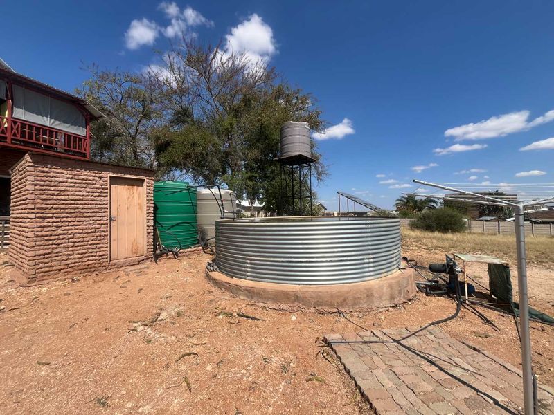 Rear exterior area featuring multiple water storage tanks, a raised tank stand, a corrugated metal reservoir, and a brick utility shed.