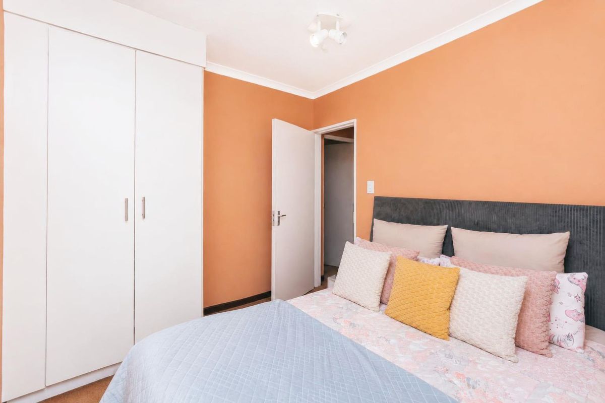 A bedroom featuring a built-in wardrobe, orange-toned walls, and a ceiling light fixture.