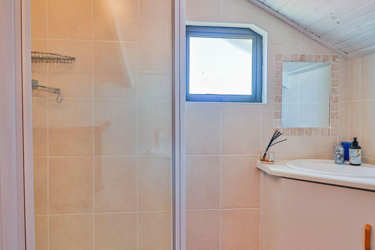 A compact bathroom featuring a shower enclosure, a built-in vanity with a basin, and a small window set under a sloped ceiling.