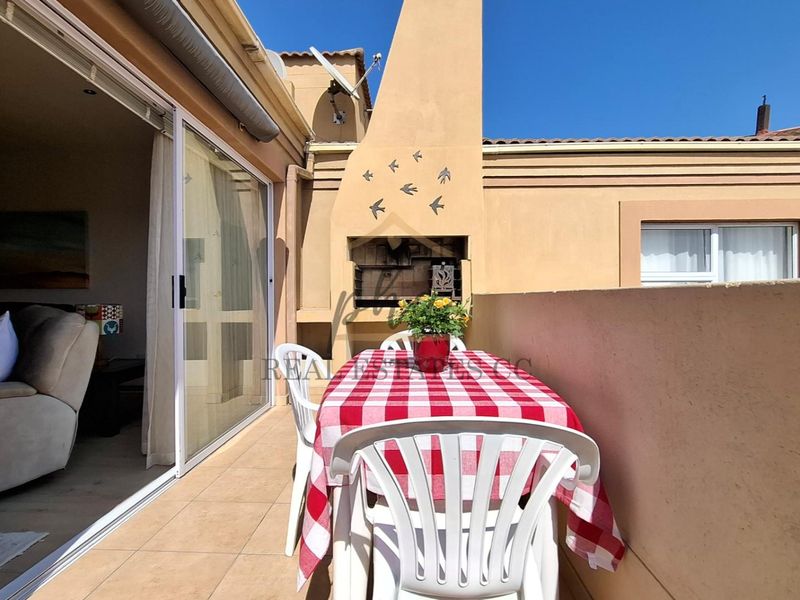 A private balcony featuring a built-in braai, tiled flooring, and direct access to the living area through large sliding glass doors.