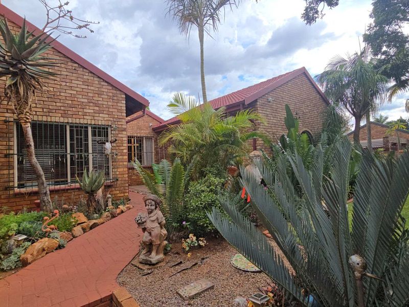 A well-maintained rear exterior view featuring a face brick facade, tiled roof, and a paved walkway leading through a landscaped garden.