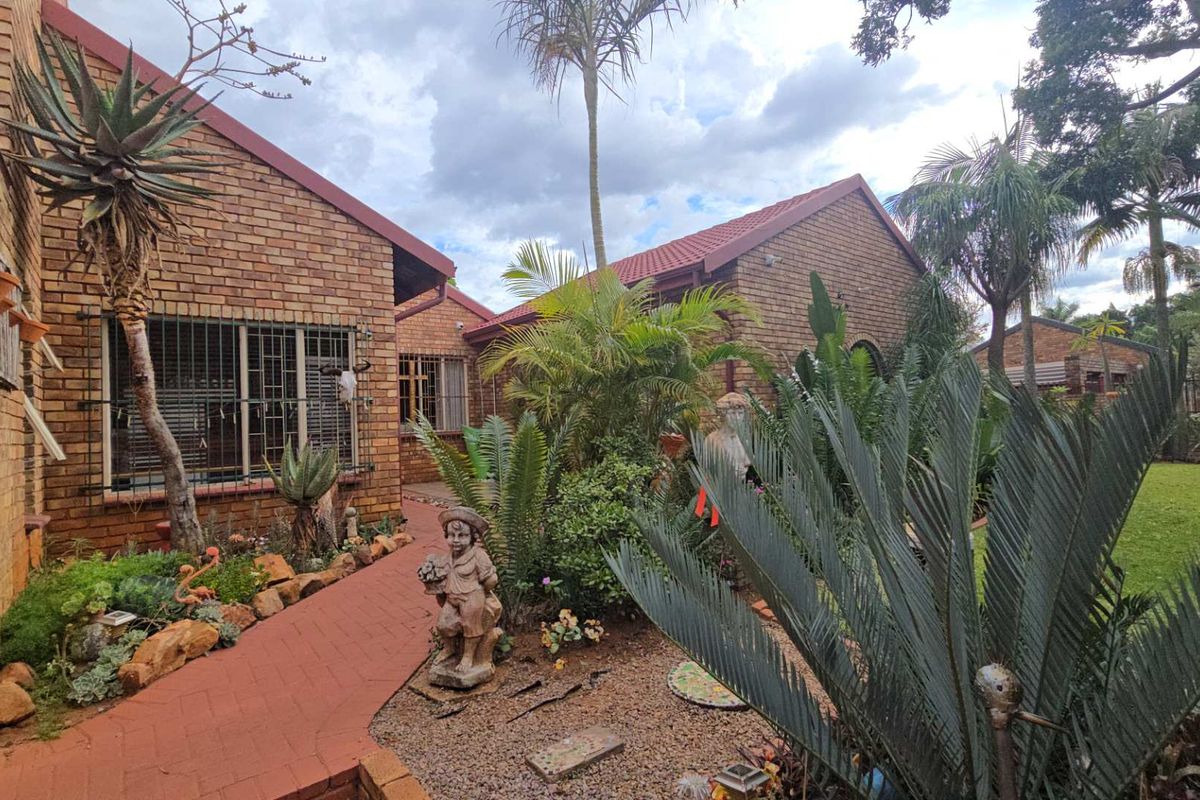 A well-maintained rear exterior view featuring a face brick facade, tiled roof, and a paved walkway leading through a landscaped garden.