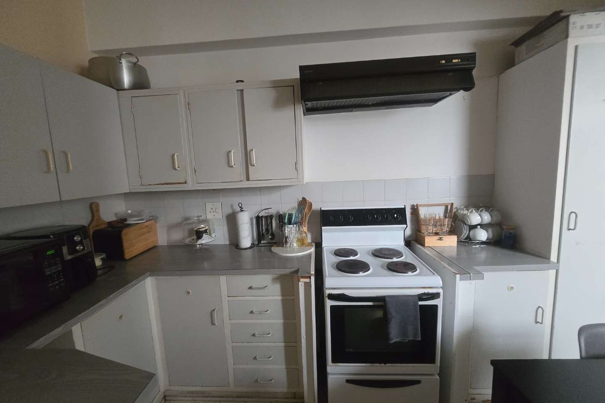 A functional kitchen featuring built-in cabinetry, a tiled backsplash, and a freestanding electric stove with an overhead extractor fan.