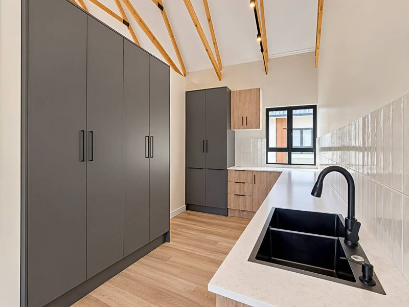 Modern scullery featuring sleek dark grey and wood-tone cabinetry, stone countertops, a double basin sink with matte black fixtures, and exposed timber rafters.