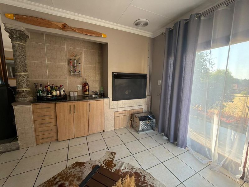 A dedicated bar area featuring built-in cabinetry, a granite countertop with sink, and a built-in fireplace, with direct access to the outdoor patio.