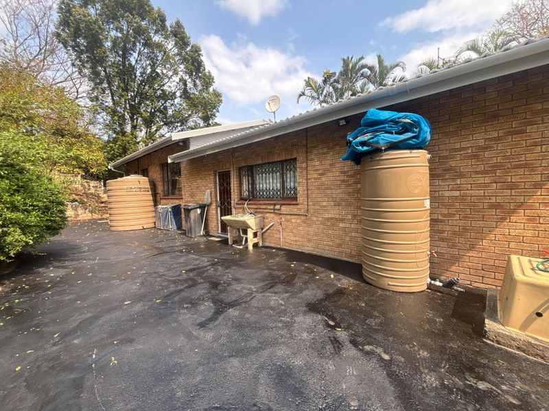 Rear exterior view of the property featuring brick facade, asphalt driveway, and multiple water storage tanks.