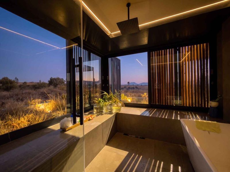 Modern luxury bathroom featuring a freestanding bathtub, rain shower, and expansive floor-to-ceiling windows offering panoramic landscape views.