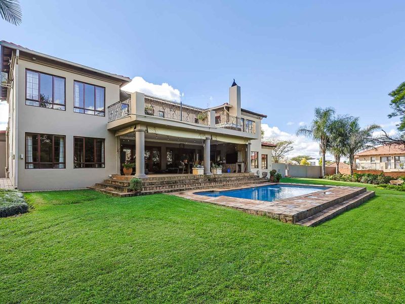 Spacious rear exterior featuring a swimming pool, raised stone patio, covered entertainment area with fireplace, and an upper-level balcony with wrought iron railings.