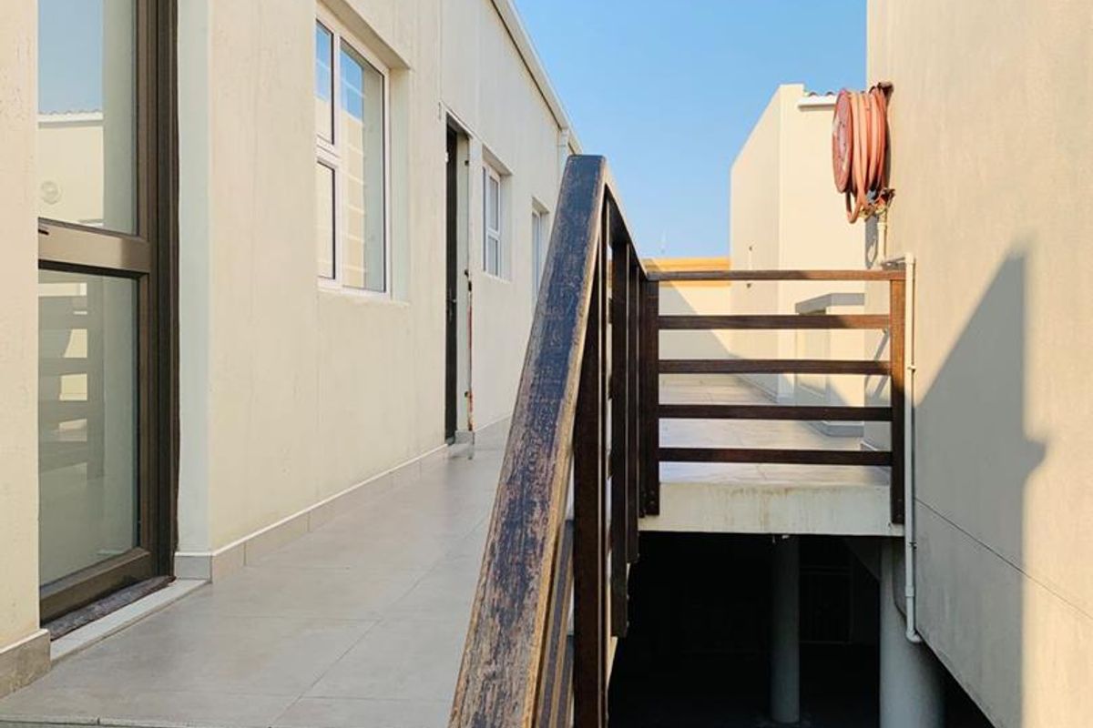 Exterior walkway featuring tiled flooring and a wooden handrail, providing access between apartment building sections.