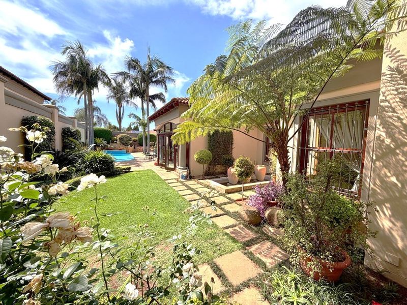 A beautifully landscaped rear garden featuring a stone paved walkway, established trees, and a swimming pool, providing a serene outdoor living space.