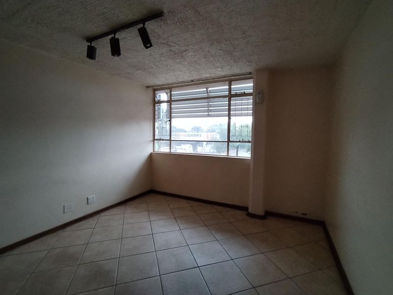 An empty living room featuring tiled flooring, track lighting, and a large window, offering a blank canvas for potential interior design and renovation.