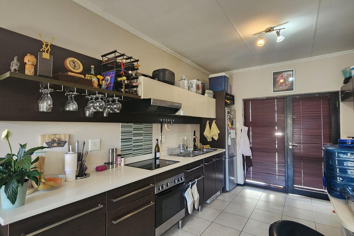 A functional kitchen featuring dark wood cabinetry, a built-in oven with hob, extractor fan, and tiled flooring with direct access to an outdoor area.