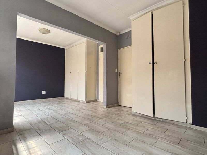 An empty bedroom featuring tiled flooring and extensive built-in cupboard storage, finished with a neutral and dark accent wall color scheme.
