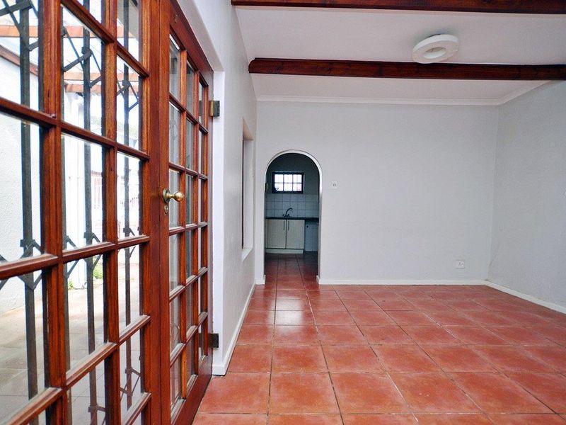 An empty living area featuring terracotta floor tiles, exposed timber ceiling beams, and timber-framed french doors leading to an outdoor space.
