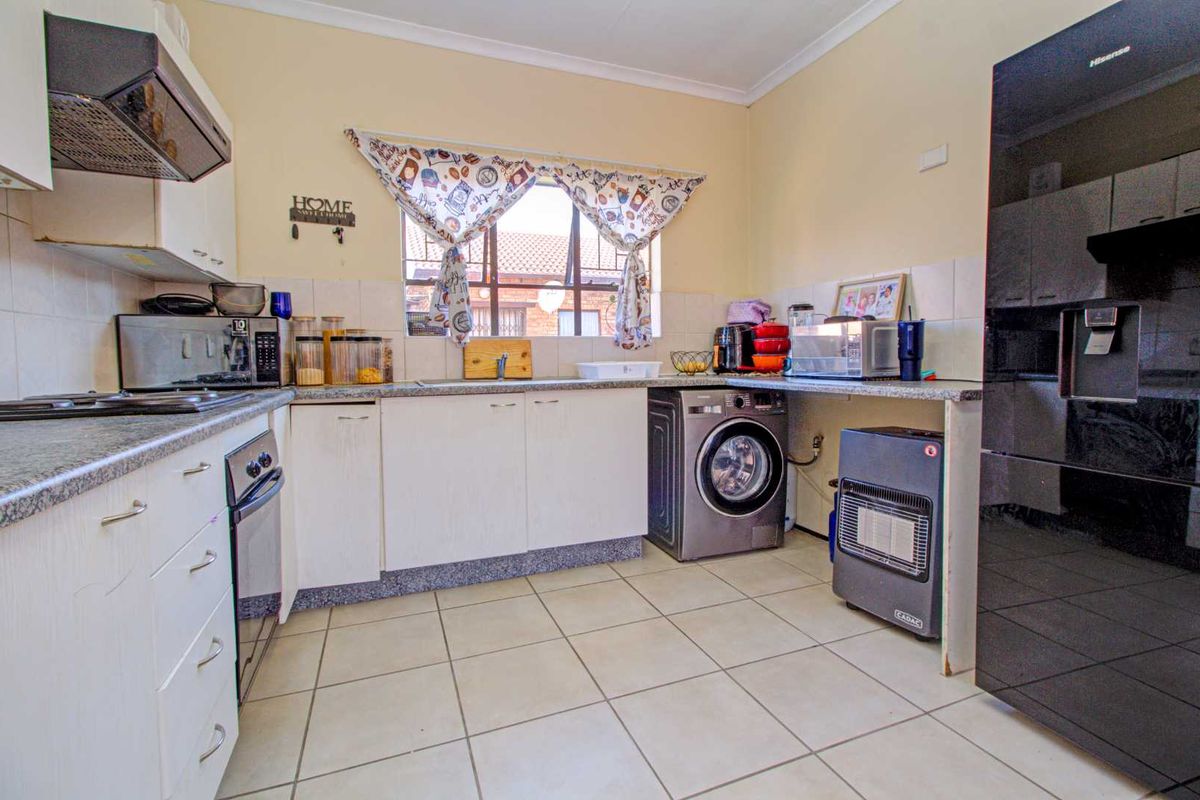 Functional kitchen featuring white cabinetry, granite-look countertops, built-in oven, extractor fan, and integrated space for a washing machine.