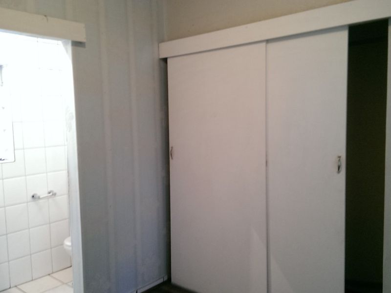 An empty office space featuring built-in sliding closet doors and an adjacent small bathroom with a pedestal sink and tiled walls.