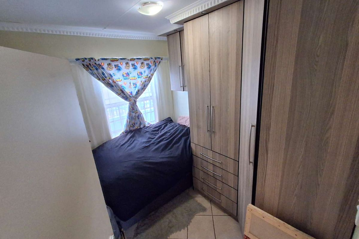 A compact bedroom featuring built-in wooden cupboards, tiled flooring, and decorative ceiling cornicing.