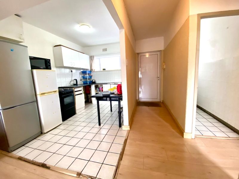 A functional kitchen area featuring tiled flooring, built-in cabinetry, and a stove, adjacent to a hallway with laminate flooring.
