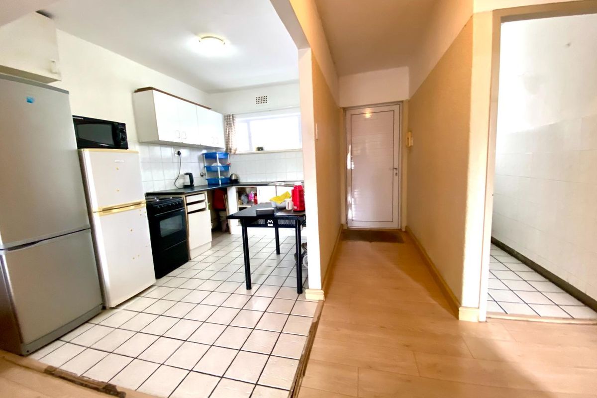 A functional kitchen area featuring tiled flooring, built-in cabinetry, and a stove, adjacent to a hallway with laminate flooring.
