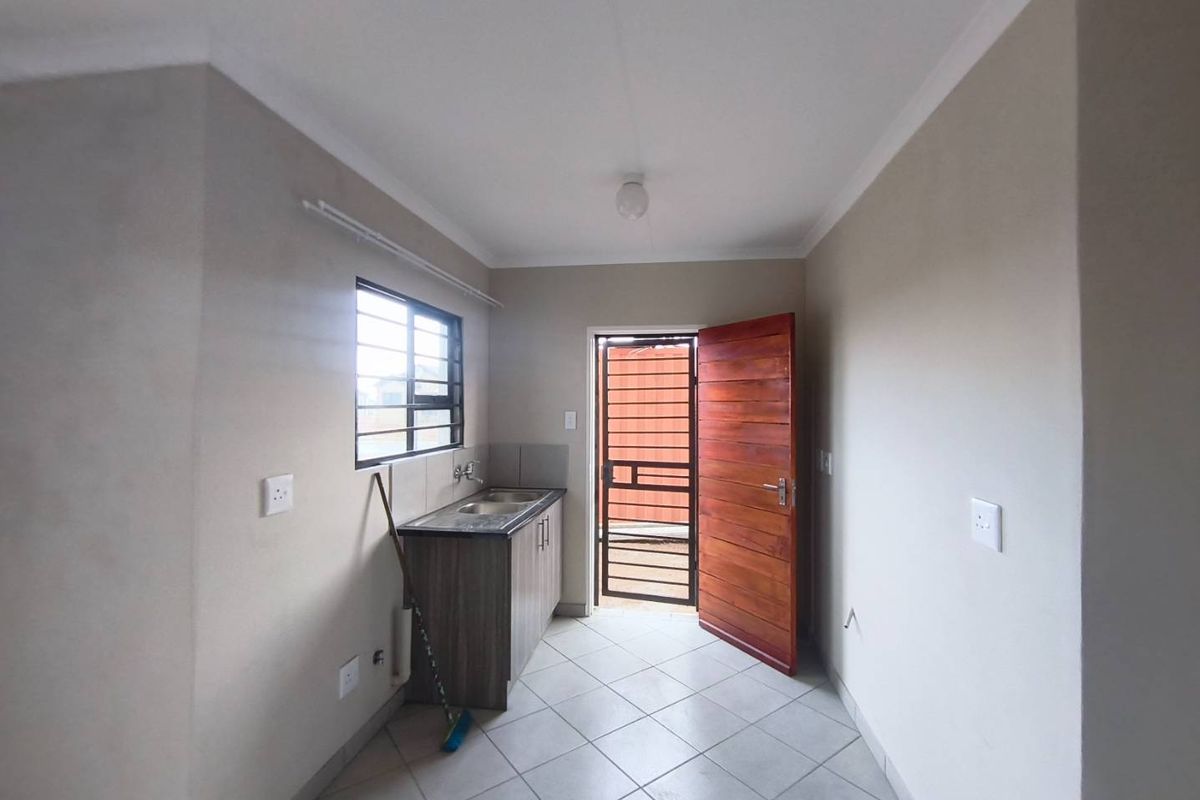 A functional kitchen area featuring tiled flooring, a single sink unit with built-in cabinetry, and direct access to the exterior via a wooden door.