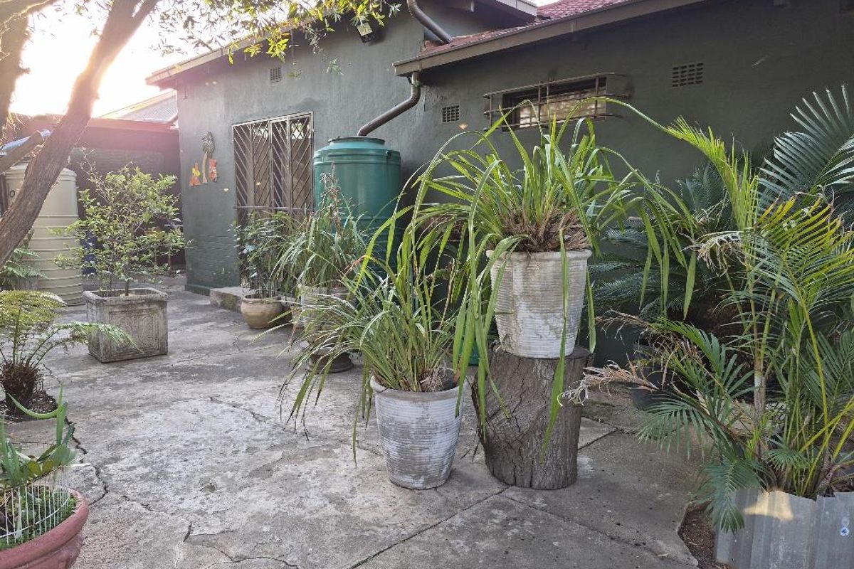 Rear exterior view of the property featuring a concrete patio area, rainwater collection tank, and security gate access.
