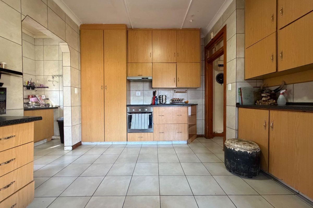 A functional kitchen featuring light wood cabinetry, built-in oven and extractor fan, tiled flooring, and a separate scullery area.