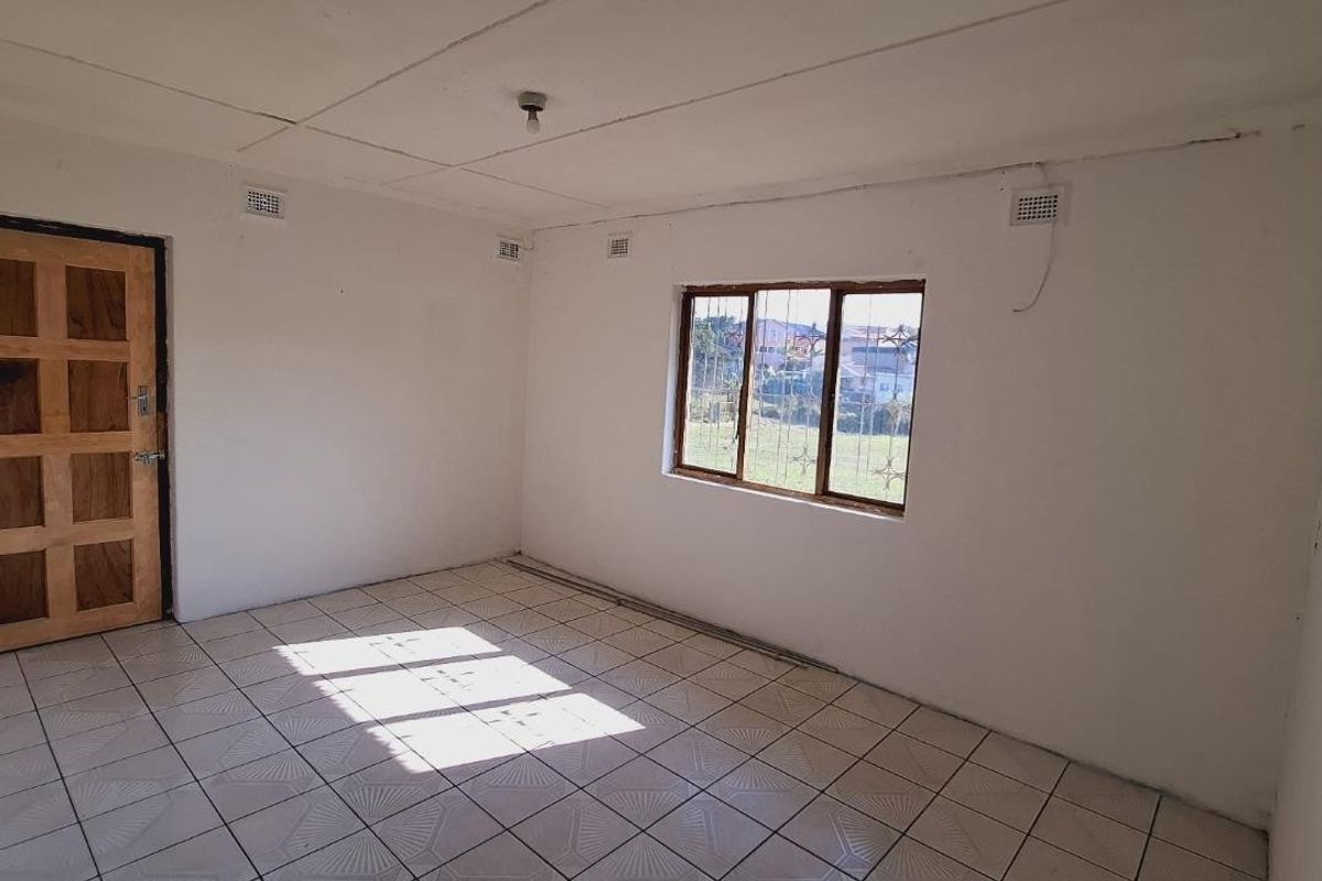 An empty living room featuring tiled flooring, a timber panel door, and security bars on the window, requiring cosmetic updates to the ceiling and finishes.