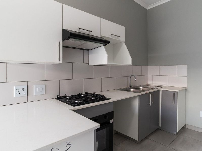 Modern kitchen featuring white and grey cabinetry, stone countertops, a gas hob, built-in oven, and a tiled backsplash.