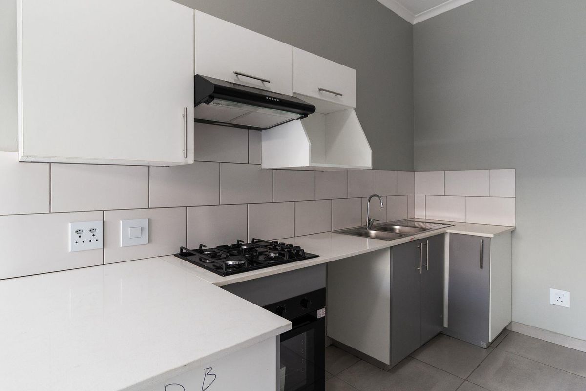 Modern kitchen featuring white and grey cabinetry, stone countertops, a gas hob, built-in oven, and a tiled backsplash.