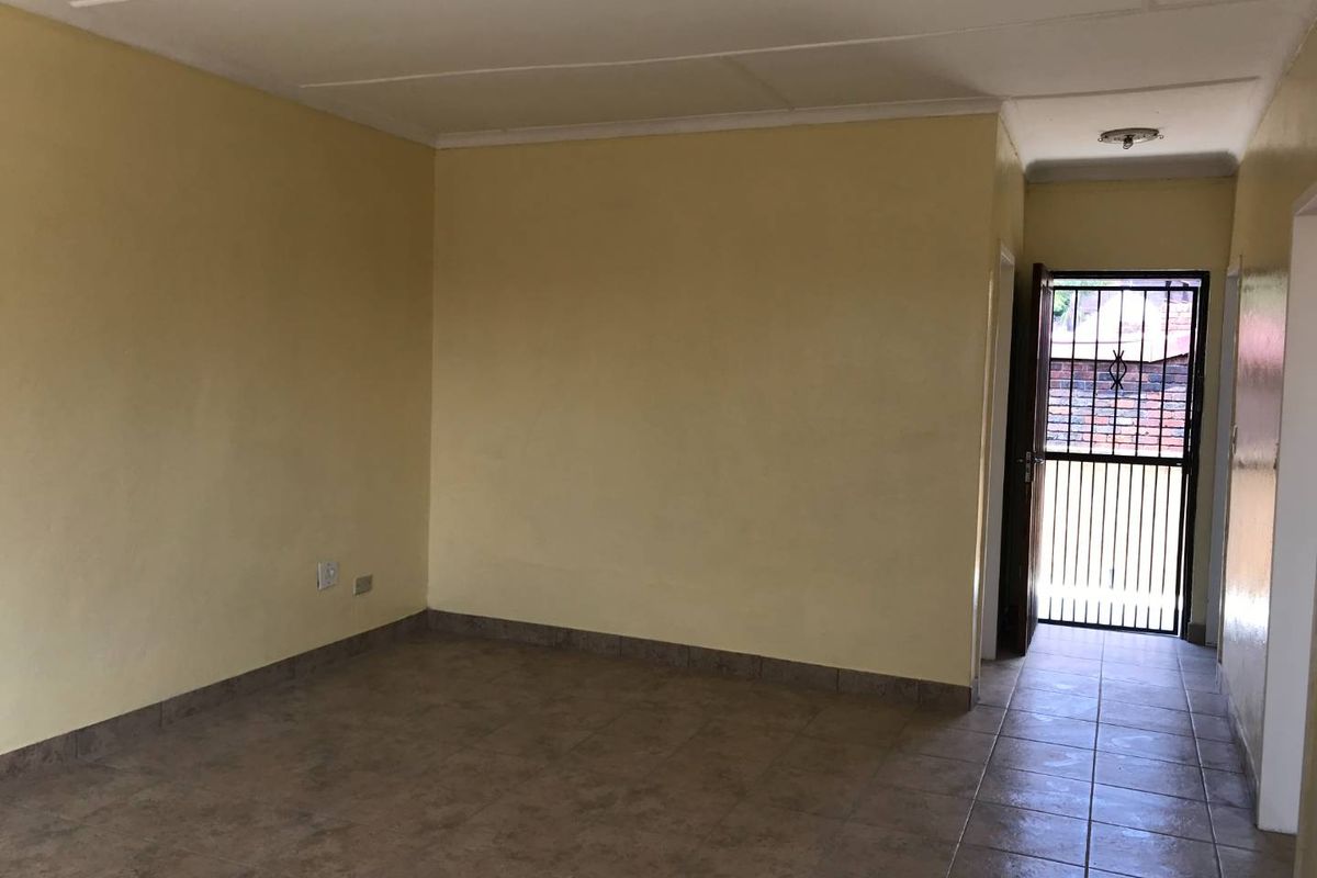 An empty living room featuring tiled flooring and a security gate entrance, providing a blank canvas for potential interior design updates.