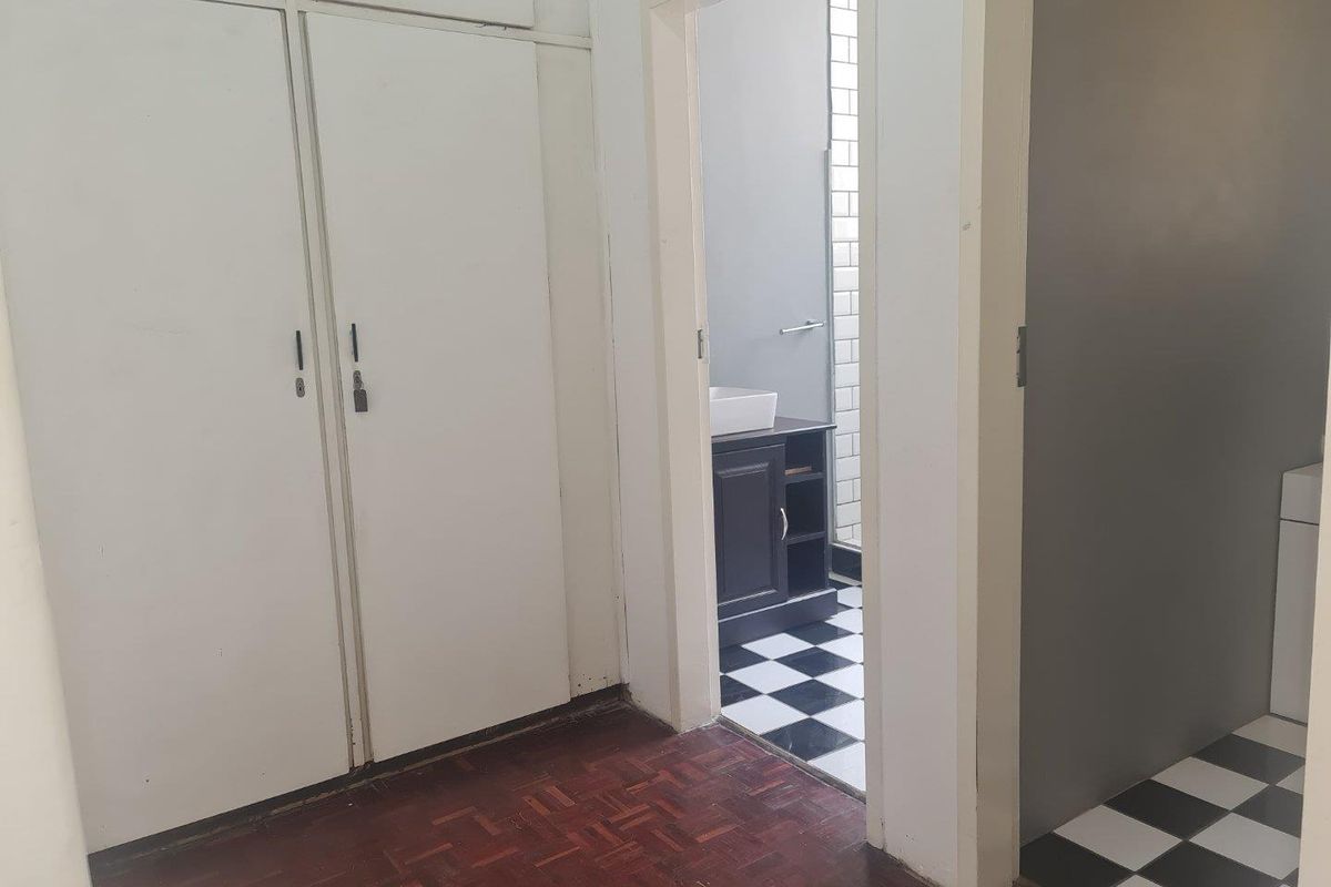 A bedroom area featuring built-in cupboards and parquet flooring, with an adjacent bathroom showcasing a modern vanity and classic black and white tiled flooring.