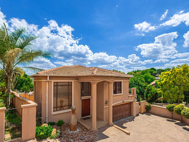 A well-maintained single-story house featuring a paved driveway, double garage, and a covered entrance with decorative columns.