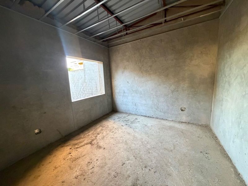 An unfinished bedroom space featuring exposed metal ceiling framing, cement rendered walls, and a concrete floor, ready for final interior finishes.