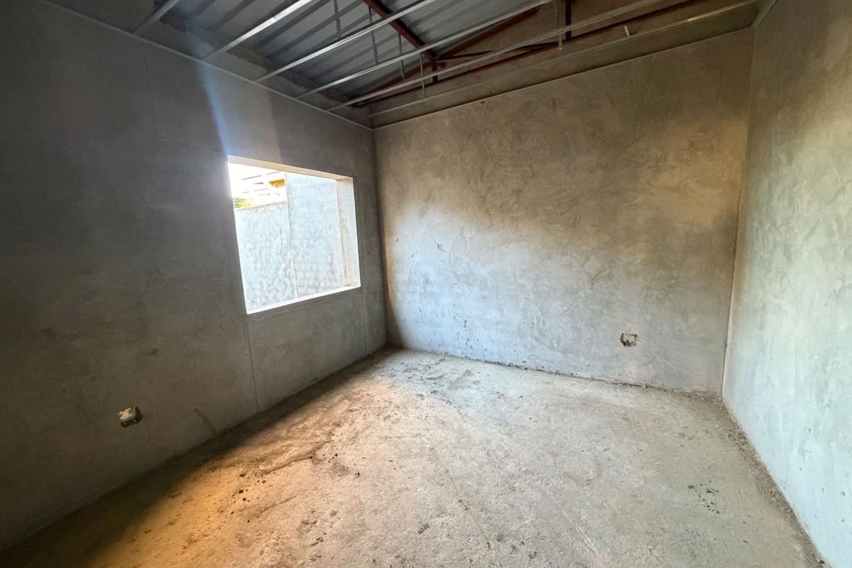 An unfinished bedroom space featuring exposed metal ceiling framing, cement rendered walls, and a concrete floor, ready for final interior finishes.