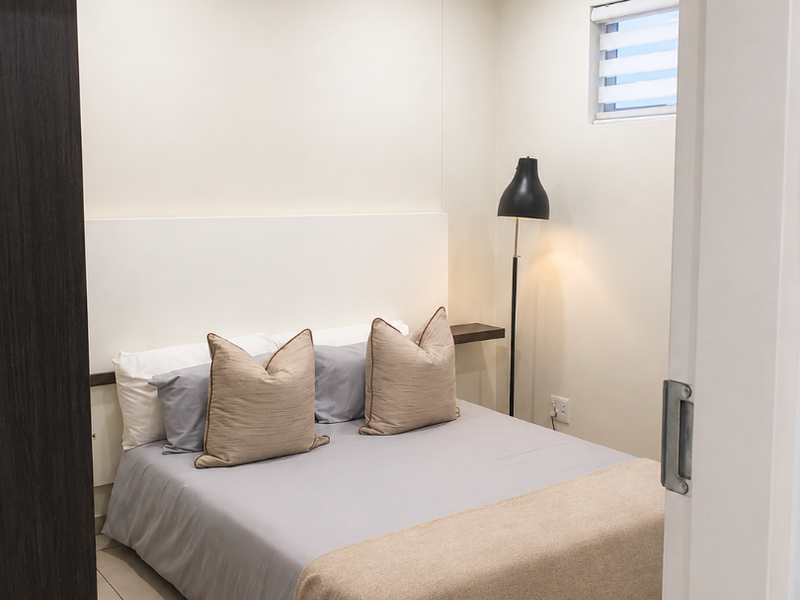 A compact, well-maintained bedroom featuring recessed lighting, a built-in headboard, and a small horizontal window, presented in a clean and modern style.