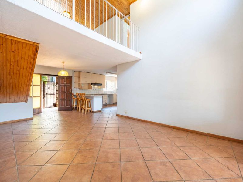 Spacious open-plan living area featuring tiled floors, a mezzanine level with a wooden ceiling, and an integrated kitchen with built-in cabinetry.