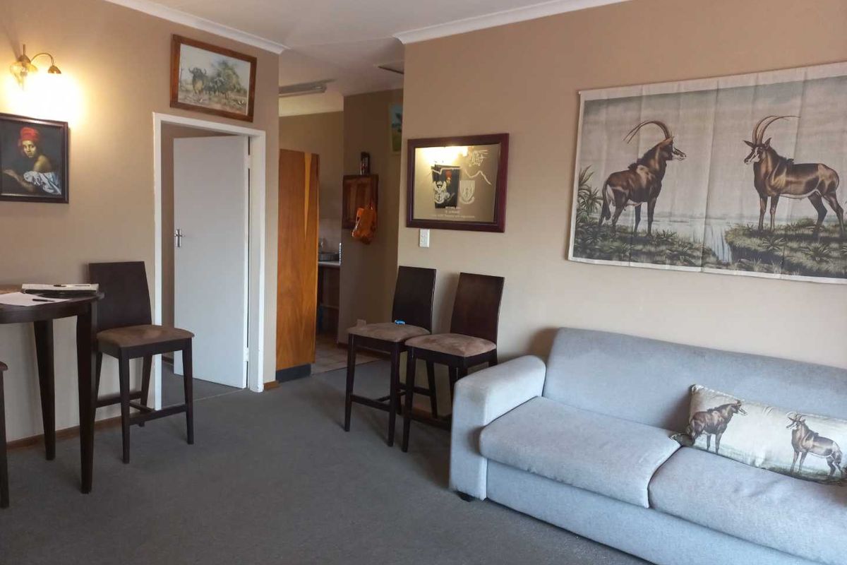 A living room area featuring neutral wall tones, carpeted flooring, and coving, providing a functional space with access to an adjacent room.