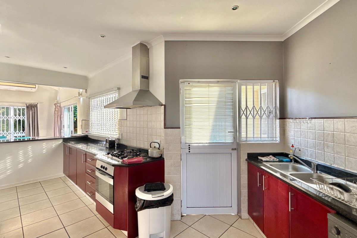 Functional kitchen featuring dark red cabinetry, granite countertops, stainless steel extractor fan, gas hob, and double basin sink with direct outdoor access.
