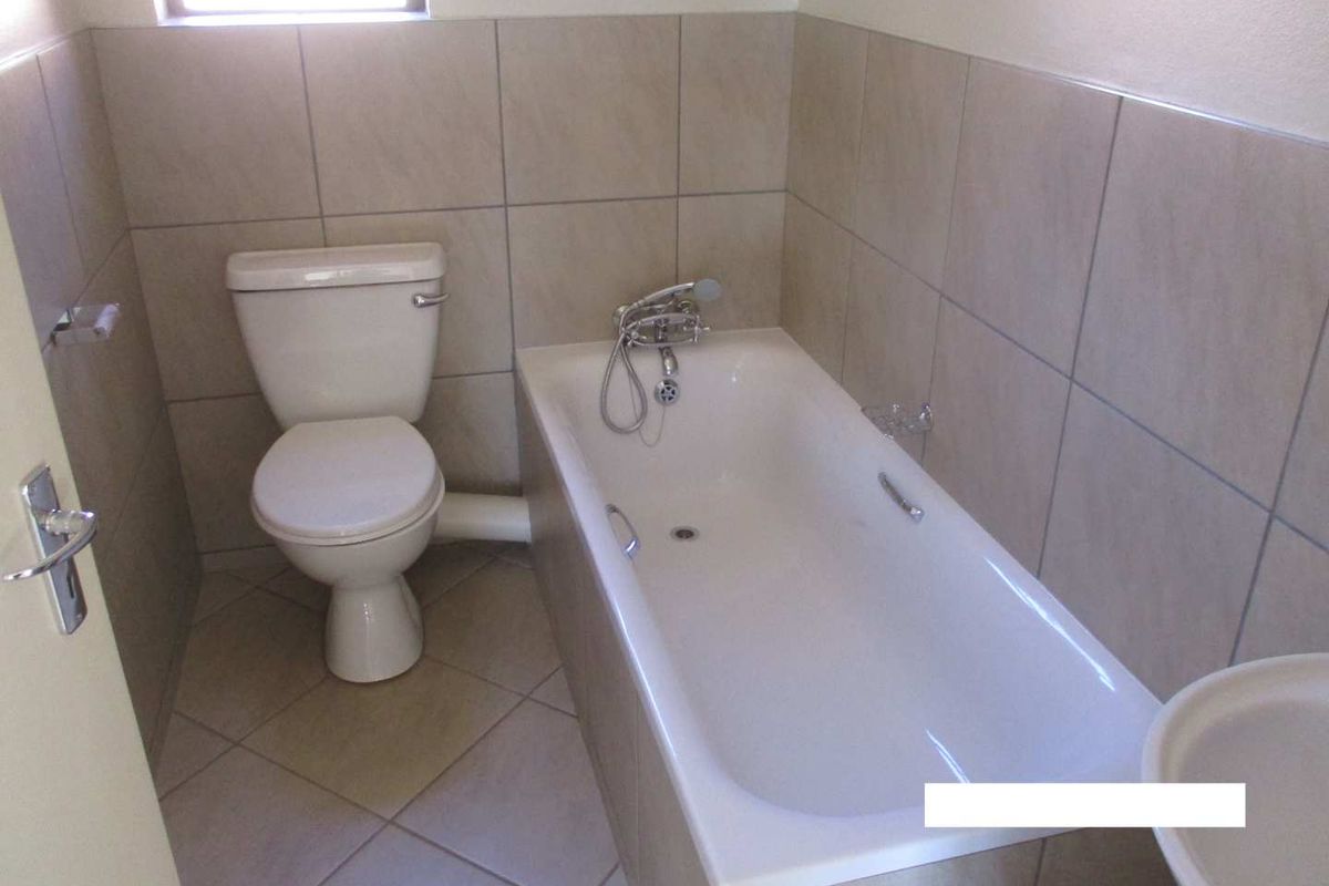A functional bathroom featuring a standard bathtub with shower mixer, toilet, and basin, finished with neutral ceramic wall and floor tiles.