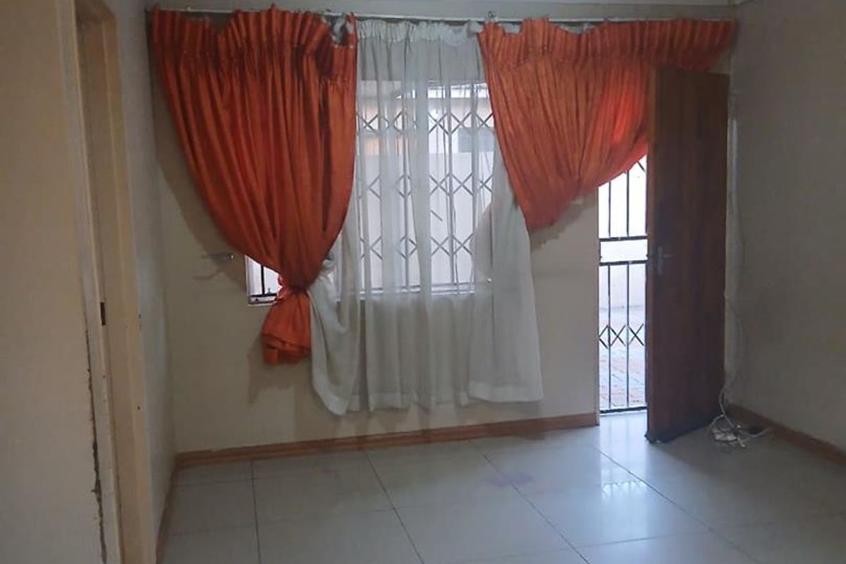 A simple, tiled living room featuring a security gate at the entrance and large windows with curtains.