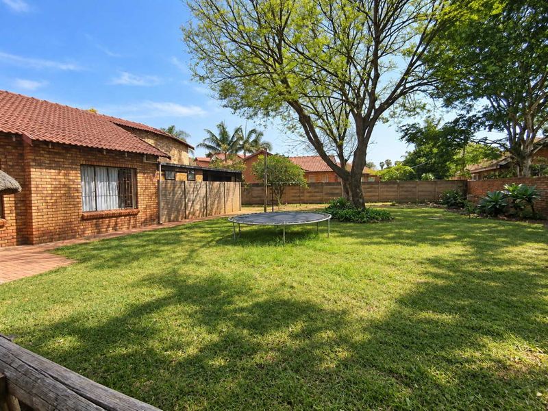 A spacious rear garden featuring a well-maintained lawn, mature trees, and a brick-faced house exterior with a tiled roof.